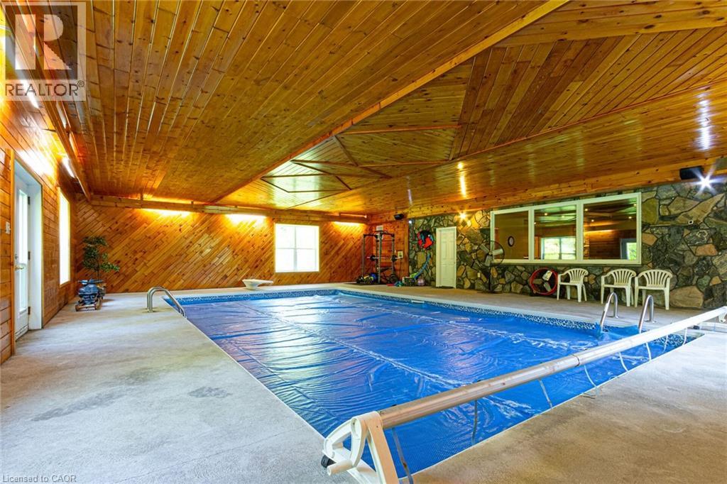 Indoor swimming pool with concrete surround, wood-paneled walls and ceiling, and a stone accent wall