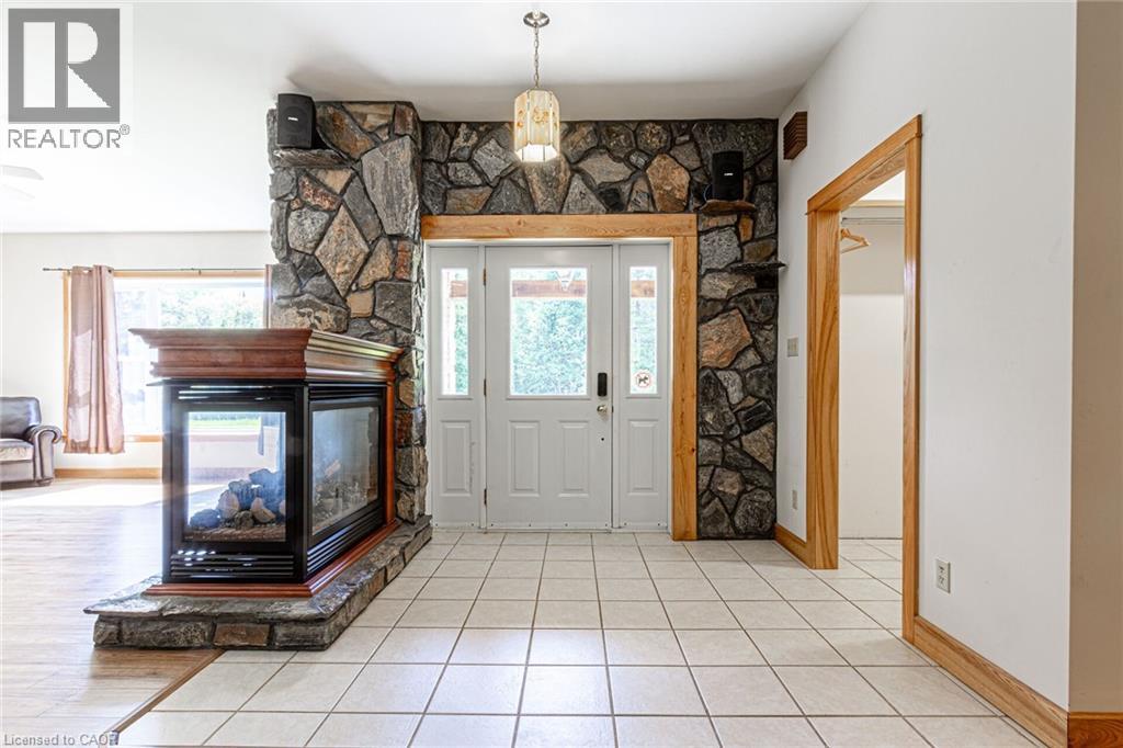 Entryway featuring a stone accent wall, double glass-paneled doors, and a built-in three-sided fireplace with a wood mantle