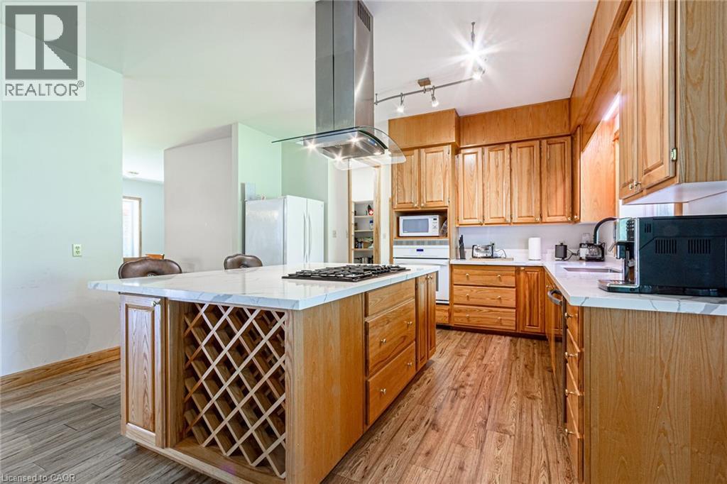 Kitchen featuring wood-finish flooring, light wood cabinetry, white countertops, a central island with integrated wine storage, and a stainless steel range hood
