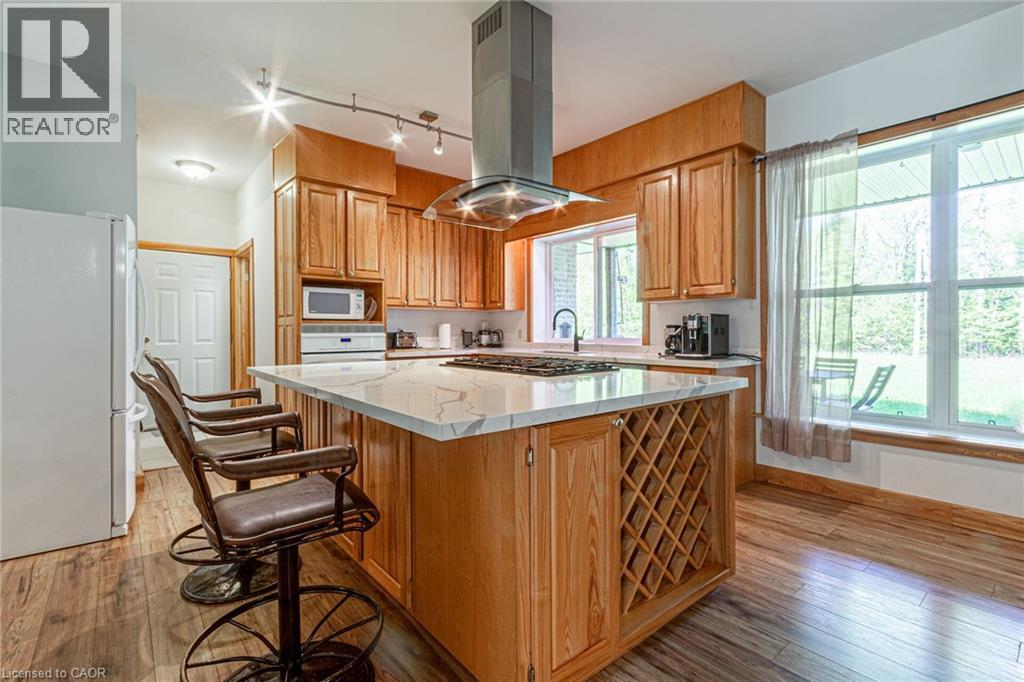 Kitchen featuring a central island with white stone-finish countertop, integrated wine rack, and a gas cooktop with a stainless steel range hood
