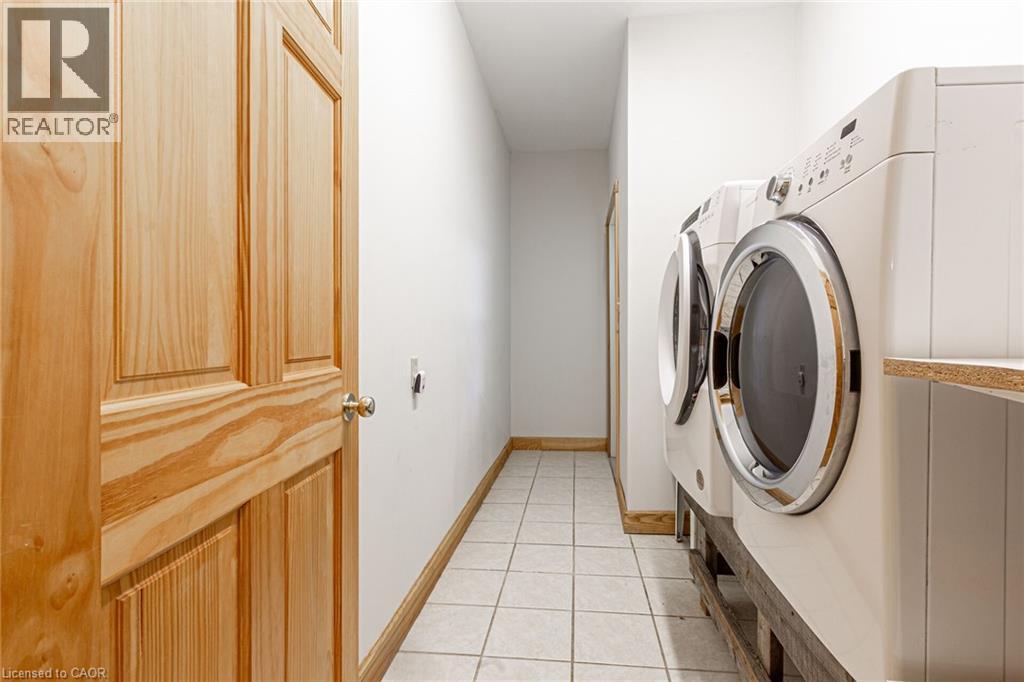 Dedicated laundry area with tile flooring, a natural wood paneled door, and wood trim baseboards
