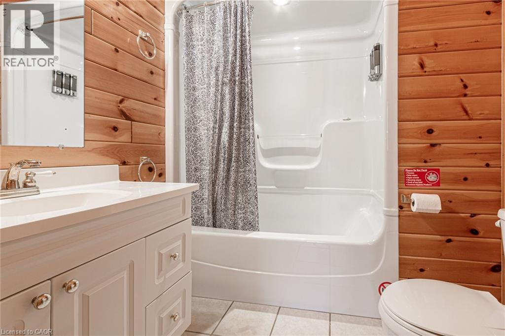Bathroom featuring wood paneling, a white vanity with integrated sink, chrome faucet, a combination bathtub and shower unit, and light-colored floor tiles