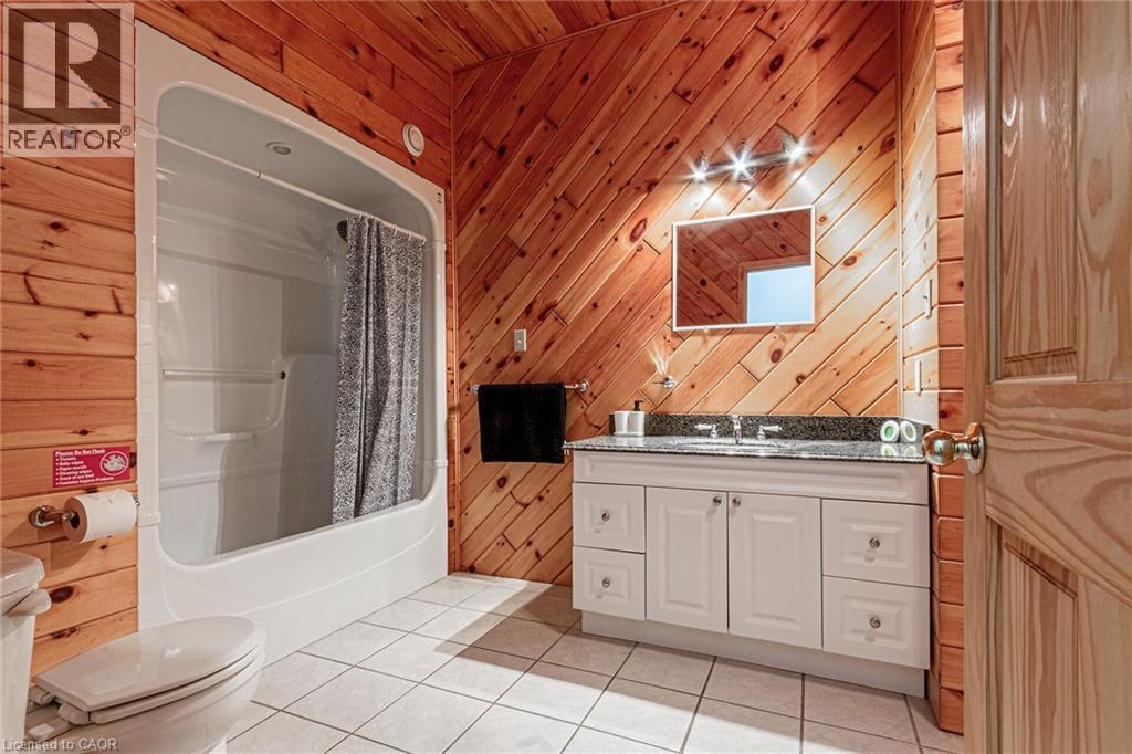 Bathroom featuring wood-finish wall paneling, white ceramic tile flooring, a white vanity with a dark countertop, and a white integrated tub and shower unit