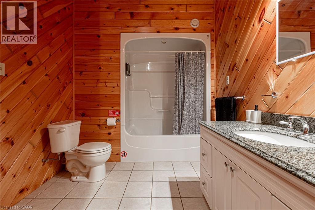 Bathroom featuring wood-paneled walls, a white vanity with a granite countertop, an integrated sink, and chrome fixtures
