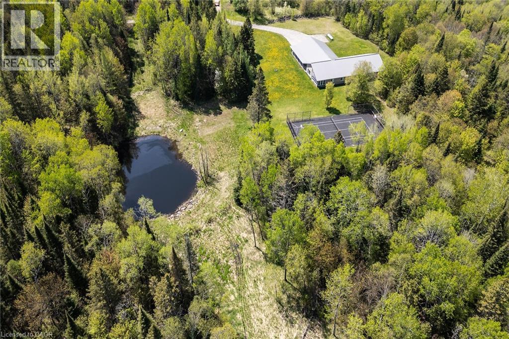 Expansive wooded property featuring a private pond, a tennis court, a long paved driveway, and a modern home with a light-colored roof