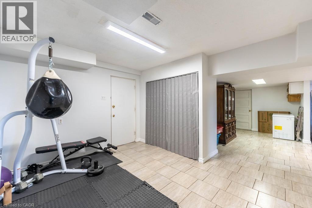Spacious lower-level room featuring light-colored tile flooring, overhead fluorescent lighting, and white painted walls
