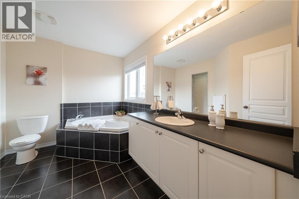 Bathroom featuring a built-in corner bathtub with black tile surround, a single vanity with a dark countertop and undermount sink, a large wall-mounted mirror, and dark diagonal floor tiling