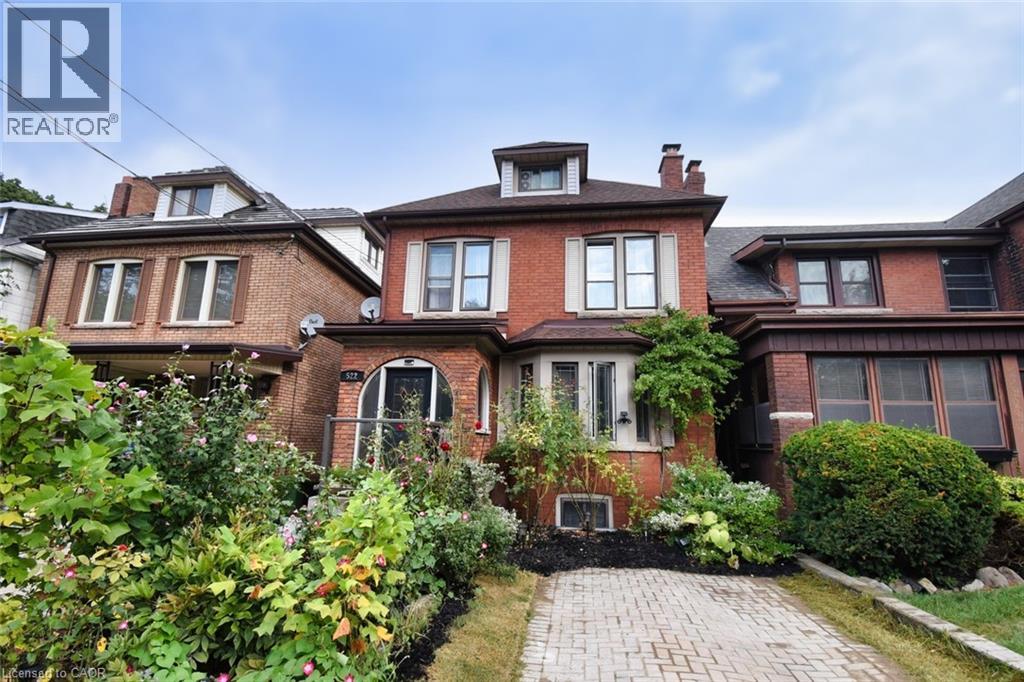 Brick exterior featuring a gabled roofline, bay windows, mature front garden, and a paver driveway