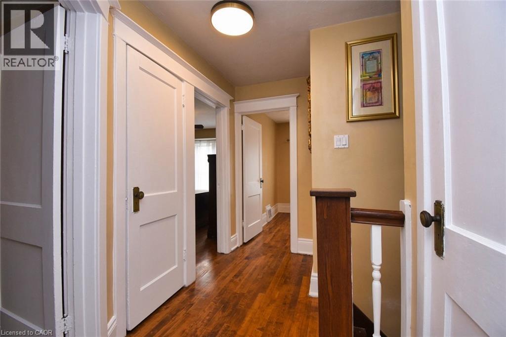 Hallway featuring wood-finish flooring, white paneled doors with bronze hardware, and a wood newel post with white balusters