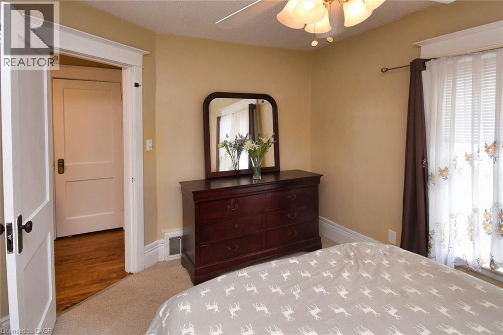 Carpeted room with a ceiling fan light fixture, a window featuring blinds and decorative curtains, and a doorway with a classic paneled door