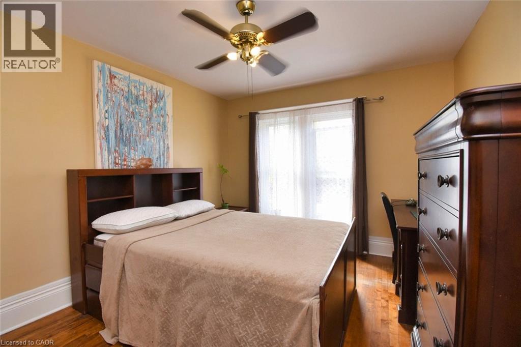 Bedroom featuring warm-toned walls, wood-finish flooring, a ceiling fan with integrated lighting, and a large window with sheer and blackout drapery