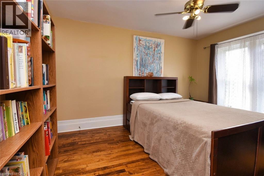 Hardwood flooring with a built-in bookcase, ceiling fan with integrated lighting, and a large window with sheer and blackout curtains