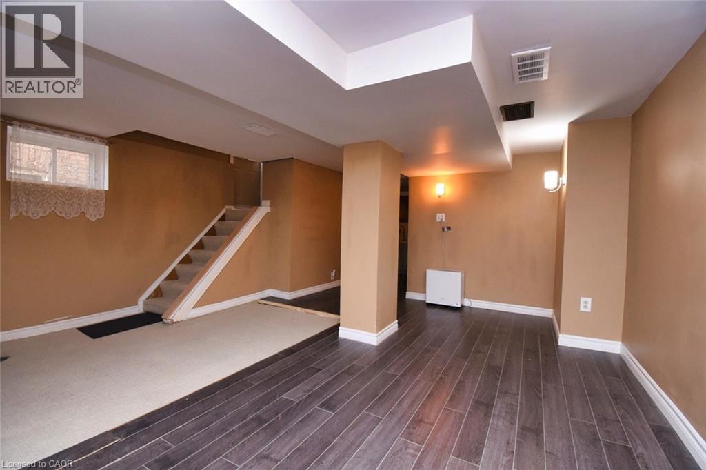 Lower-level room featuring wood-finish flooring, a carpeted stairwell, and a window with brick exterior visible
