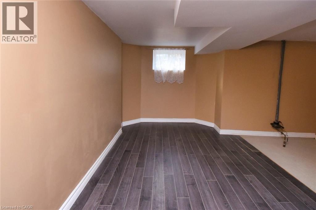 Interior space featuring wood-finish flooring, light tan wall paint, white baseboards, and a window with white curtains