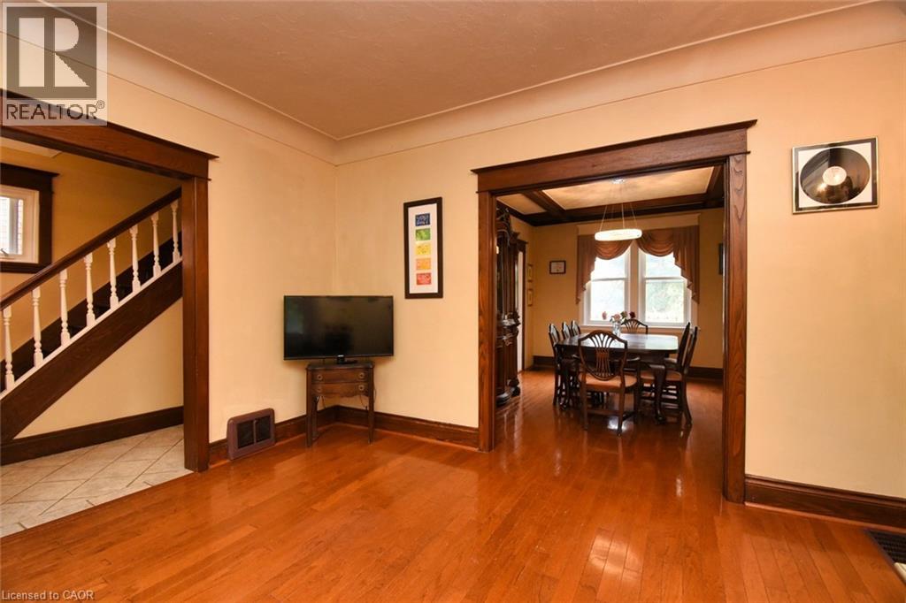 Spacious interior featuring warm wood-finish flooring, substantial dark wood trim, a wide doorway opening, a staircase with white balusters, and a visible dining area with a tray ceiling