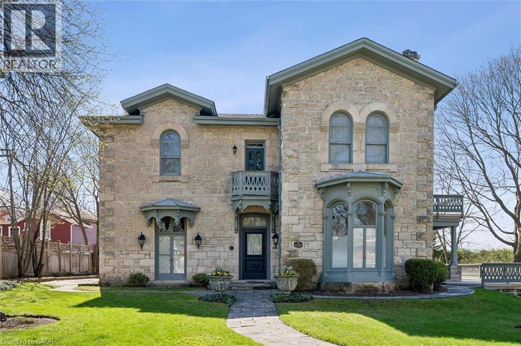 Stone exterior residence featuring a prominent bay window, arched window details, a decorative second-story balcony, and a stone walkway leading to the entry