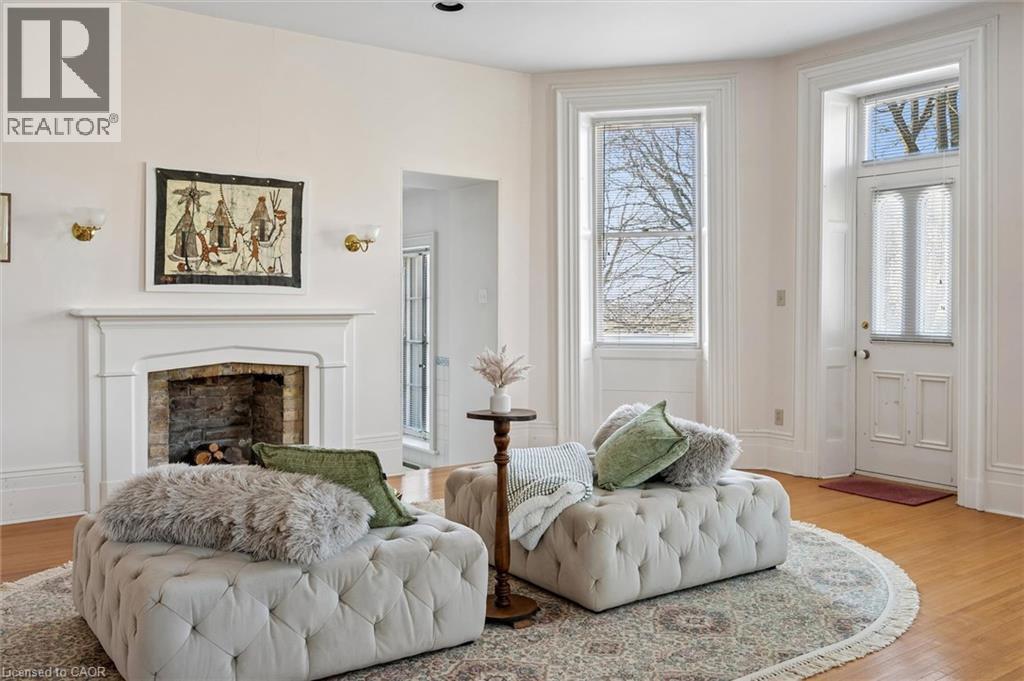 Living space featuring a white mantel fireplace with a stone-lined firebox, light wood-finish flooring, and a decorative entry door with a transom window