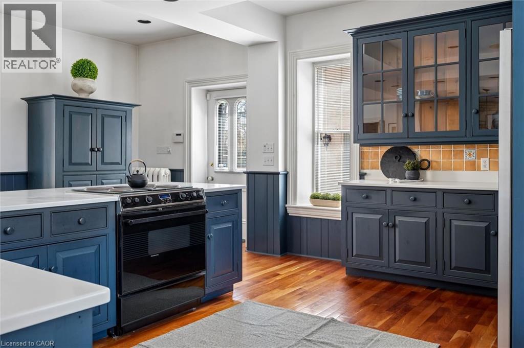 Kitchen featuring blue shaker-style cabinetry, wood-finish flooring, white countertops, built-in oven with electric cooktop, and a tiled backsplash