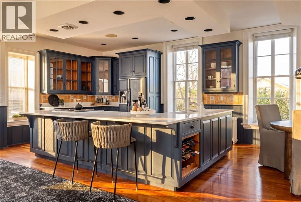 Spacious kitchen featuring an expansive central island with integrated wine storage, recessed lighting, hardwood flooring, ample cabinetry with glass-front accents, and multiple large windows