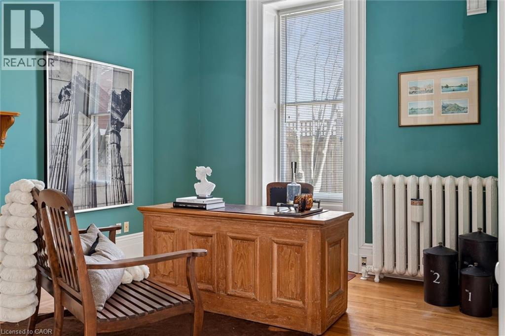 Hardwood flooring and teal painted walls define this room, featuring a large window with white trim, a classic white radiator, and a substantial wood-paneled desk