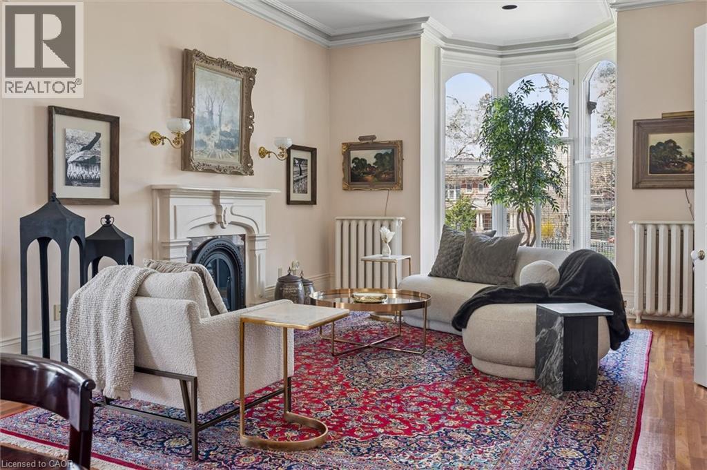 Bay windows with arched top panes, crown molding, a decorative fireplace with a mantel, wall sconces, and hardwood flooring
