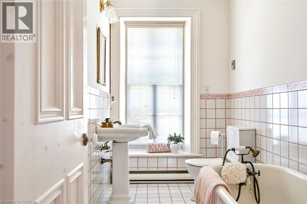 Bathroom featuring a pedestal sink, a clawfoot tub with vintage-style fixtures, and white square wall tiles with decorative trim