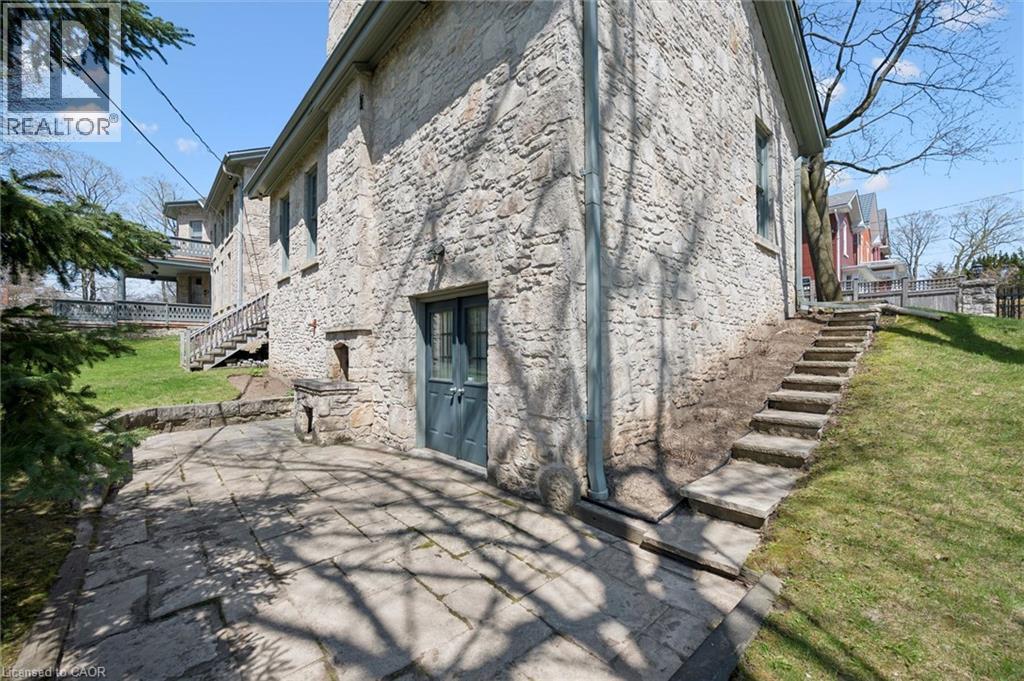 Stone patio with a textured stone exterior, featuring a double-door entry, exterior stone steps, a stone retaining wall, and a sloped lawn
