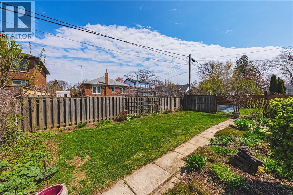 Expansive grassy lawn surrounded by a privacy fence, concrete pathway, and mature plantings