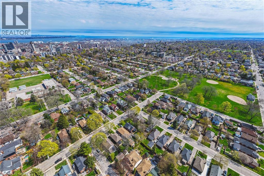 Aerial perspective showcasing a residential area featuring established homes, verdant parkland, and an expansive cityscape with distant water