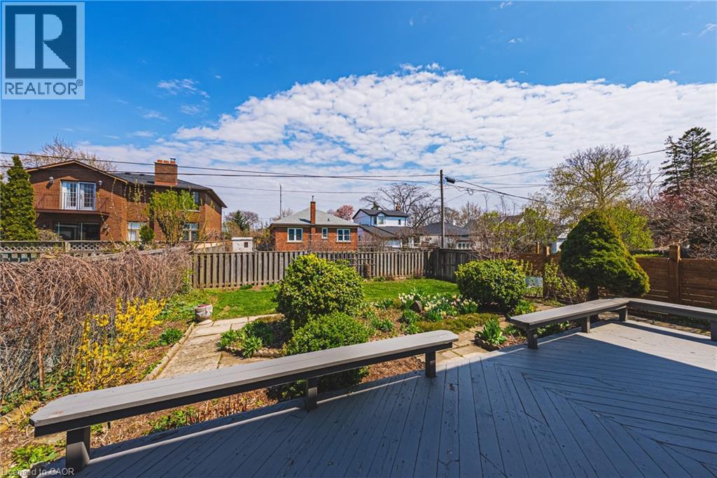 Expansive backyard featuring a multi-level wood deck with built-in benches, a manicured lawn, established garden beds, and perimeter fencing