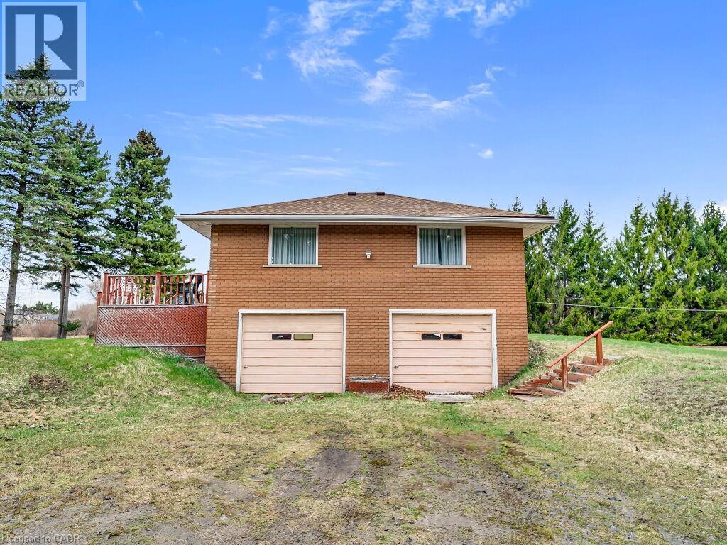 Brick exterior residence featuring two garage bays, a side deck with railing, and a sloped grassy area