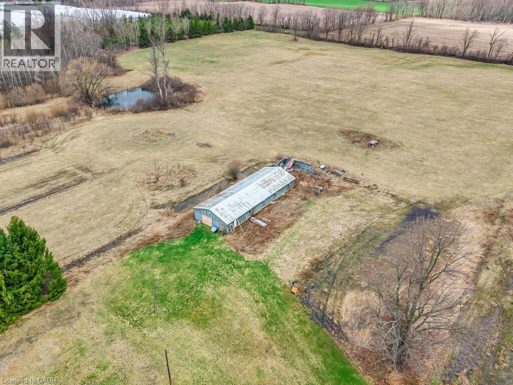 Expansive agricultural land featuring a lengthy outbuilding, a natural pond, and scattered mature trees