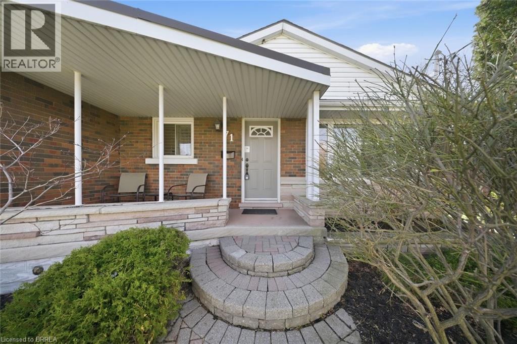 Brick facade home featuring a covered front porch, stone veneer accents, an arched paver stone pathway, and mature landscaping