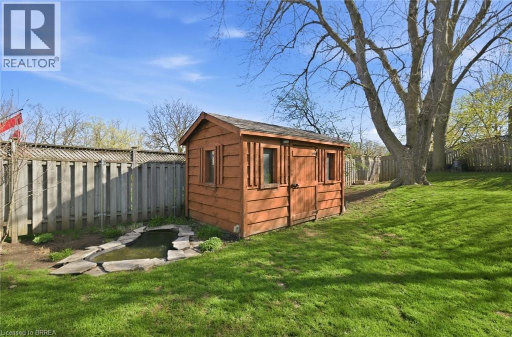 Expansive grassy backyard featuring a wooden shed, a stone-edged pond, a tall privacy fence, and mature trees