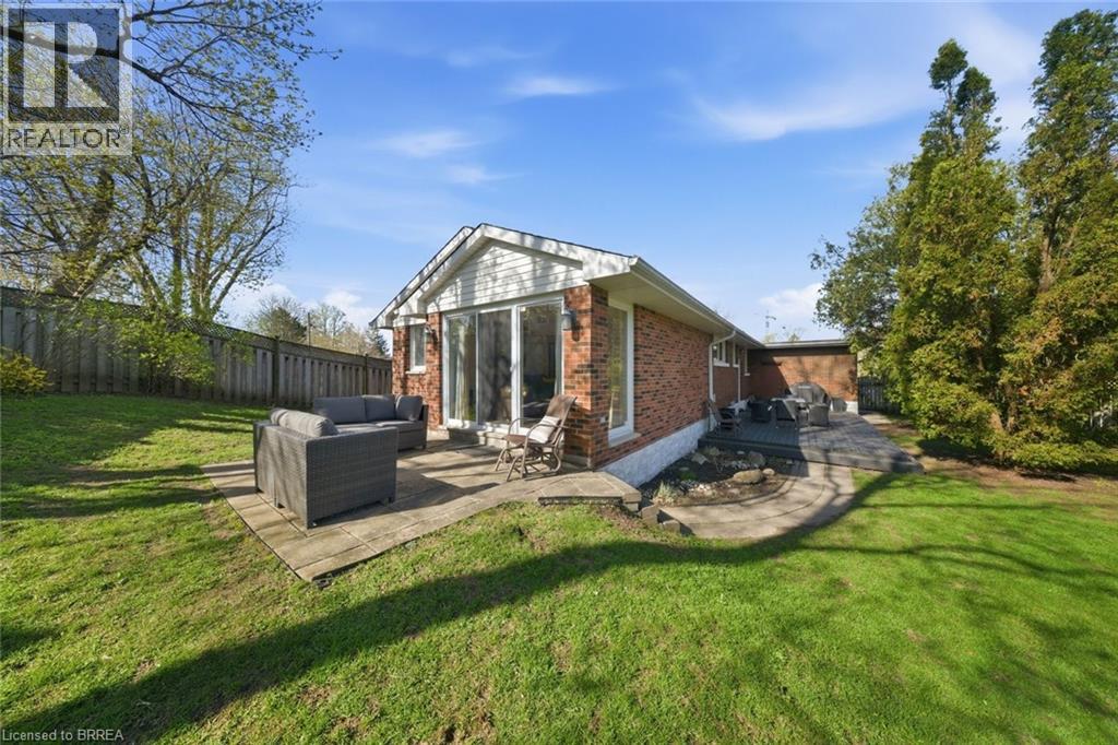Expansive rear yard featuring a manicured lawn, two distinct patio areas, and a brick exterior with white siding accents