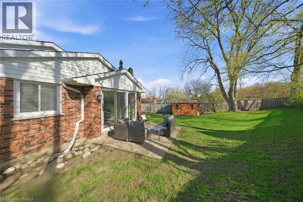 Expansive backyard featuring a large concrete patio, manicured lawn, mature trees, and a wood-paneled shed