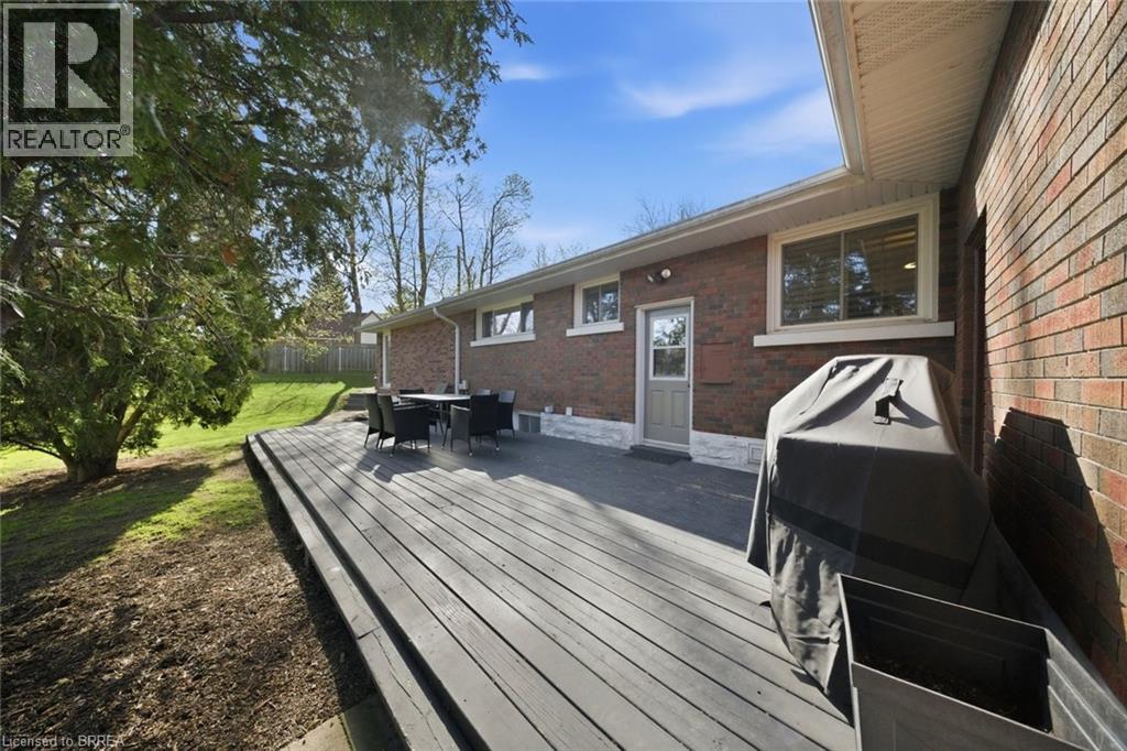 Expansive multi-level wood deck featuring a brick exterior, white trim windows, a rear entrance door, and a sloping green lawn