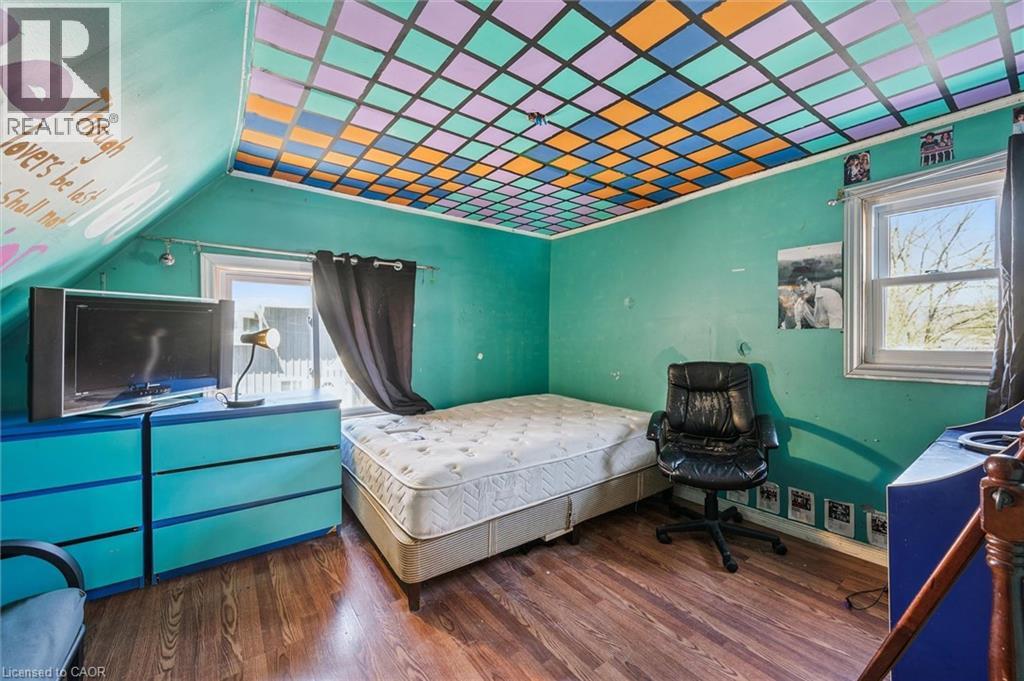 Room featuring wood-finish flooring, a colorful geometric patterned ceiling, a sloped ceiling with painted script, and a window with a dark curtain