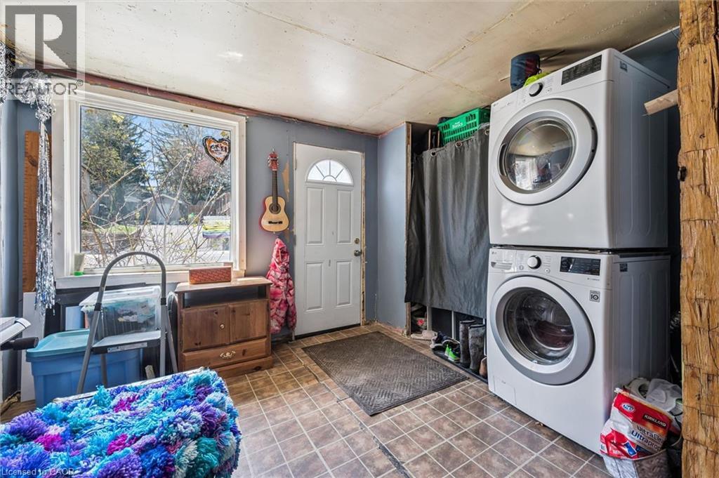 Utility area featuring a window, exterior door with a half-moon transom, stacked washer and dryer, and wood-finish flooring
