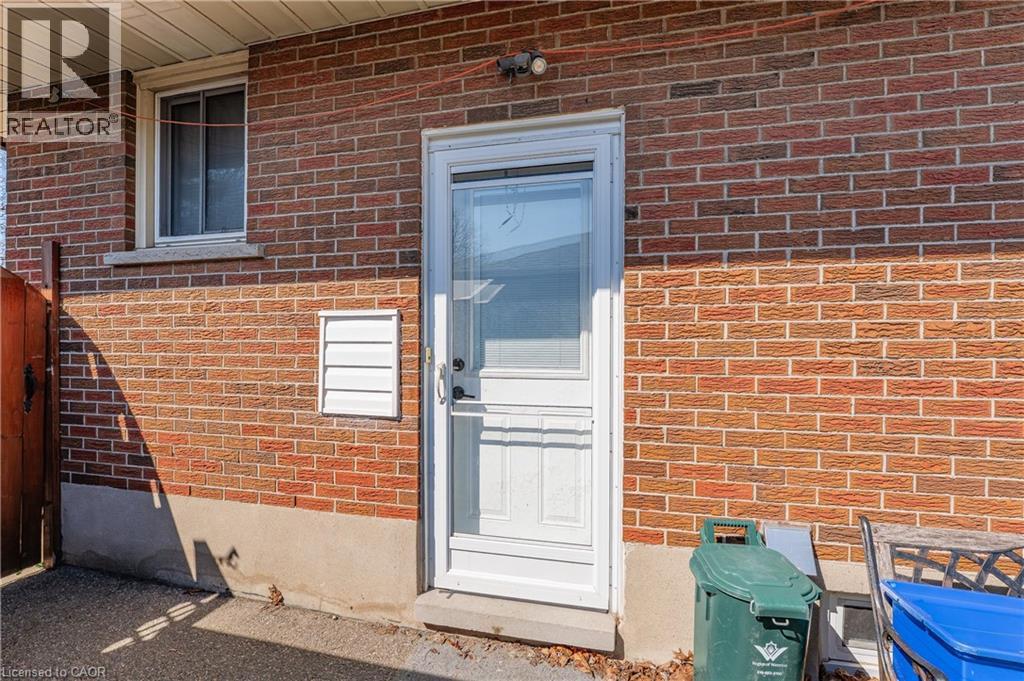 Red brick exterior featuring a white door with full-light storm door, an overhead light fixture, and a white window with a stone sill