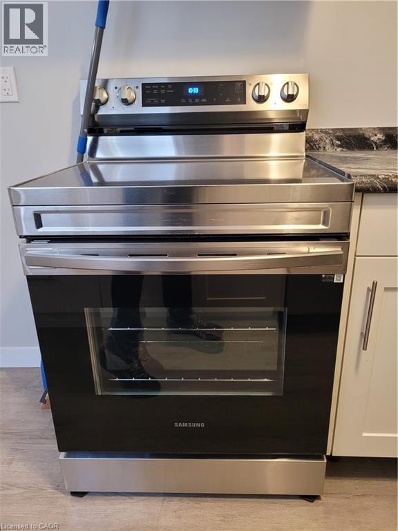 Stainless steel range with a black glass cooktop and front controls, featuring an integrated oven with a visible interior rack, set against a dark speckled countertop and light cabinetry