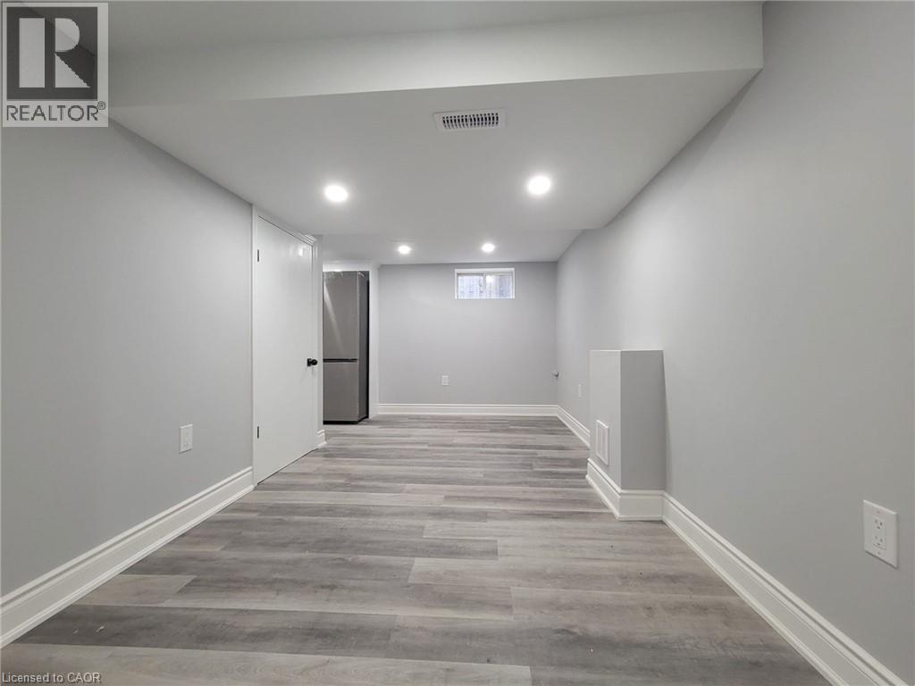 Spacious room featuring light gray walls, wood-finish flooring, recessed ceiling lighting, and white baseboards