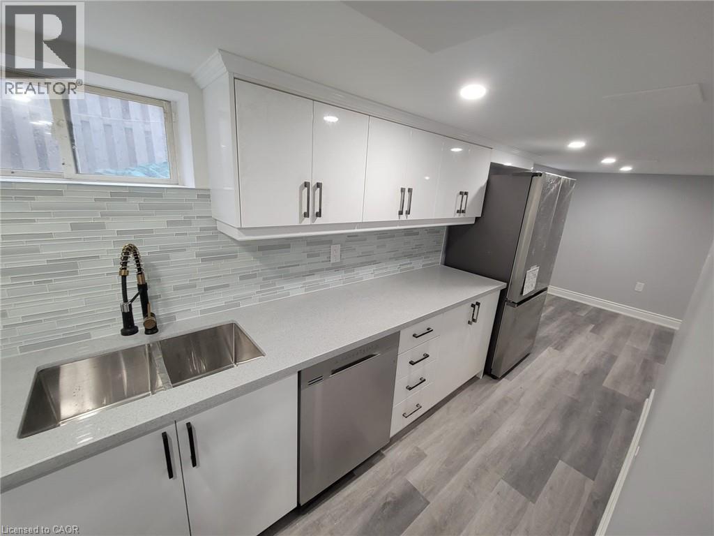 Modern kitchen featuring white cabinetry, light gray countertops, a stainless steel double sink with a flexible faucet, a matching dishwasher, and a refrigerator