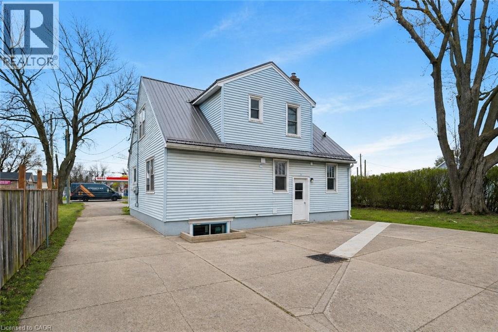 Light blue horizontal siding and a gray metal roof define this property, featuring multiple windows, a concrete driveway, and a wooden privacy fence