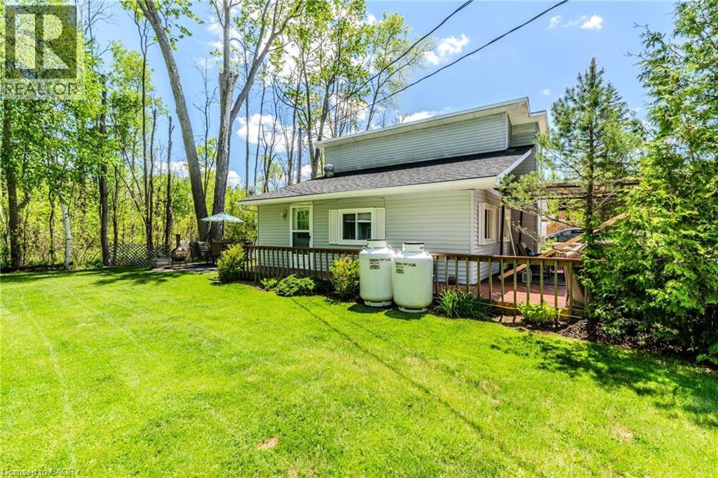 Spacious rear yard with green lawn, bordered by mature trees and natural foliage