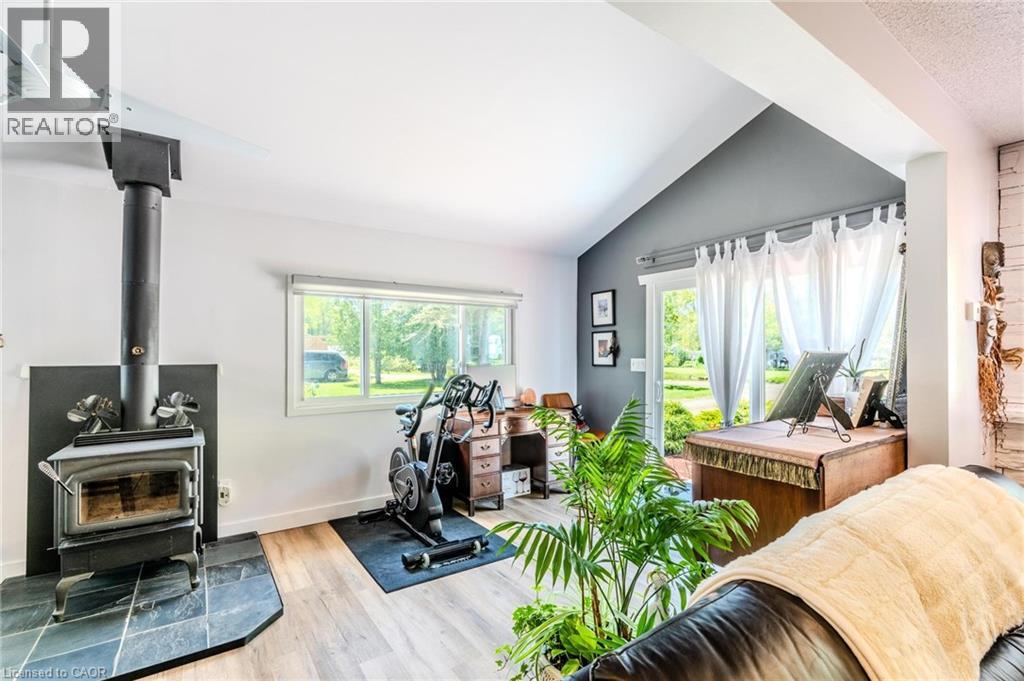 Vaulted ceilings highlight this versatile room featuring a wood-burning stove with a slate hearth, wood-finish flooring, and a large picture window