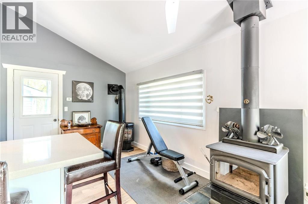 Vaulted ceiling room featuring a sleek wood-burning stove, a bright window with horizontal blinds, and a white countertop island
