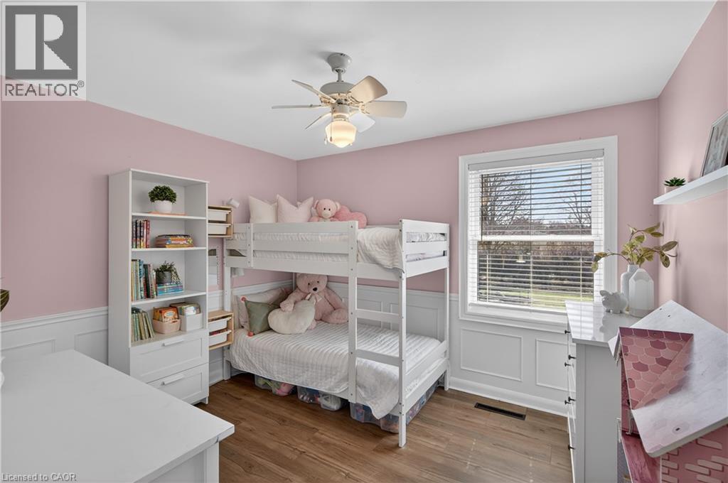 Room featuring wood-finish flooring, a double-pane window with horizontal blinds, wainscoting details, and a ceiling fan with integrated lighting