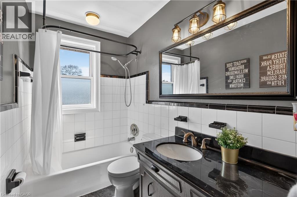 Bathroom featuring a white subway tile surround with black trim, a bathtub with a shower kit, and a large vanity with a dark countertop and undermount sink