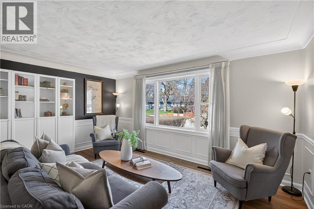 Living area featuring wood-finish flooring, an expansive picture window with bright natural light, built-in cabinetry with glass display doors, and detailed crown molding with wainscoting